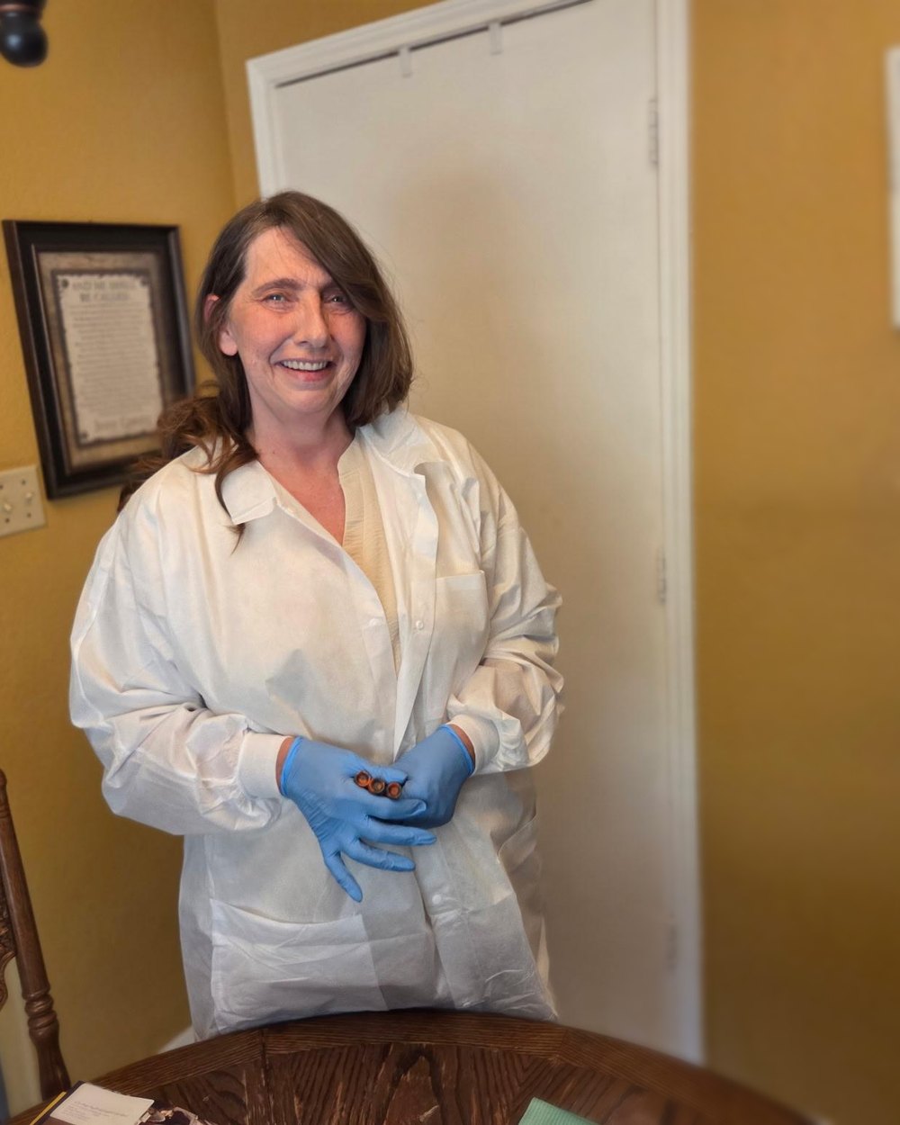 Mary Bratcher smiling during a home visit, holding labeled specimen tubes